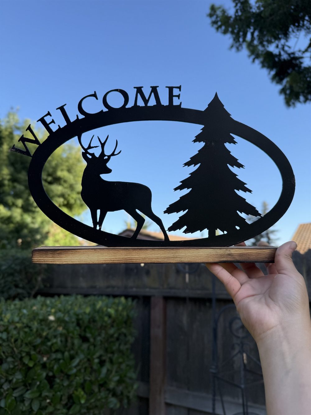 A steel WELCOME sign with a buck and pine tree, on a wood base.