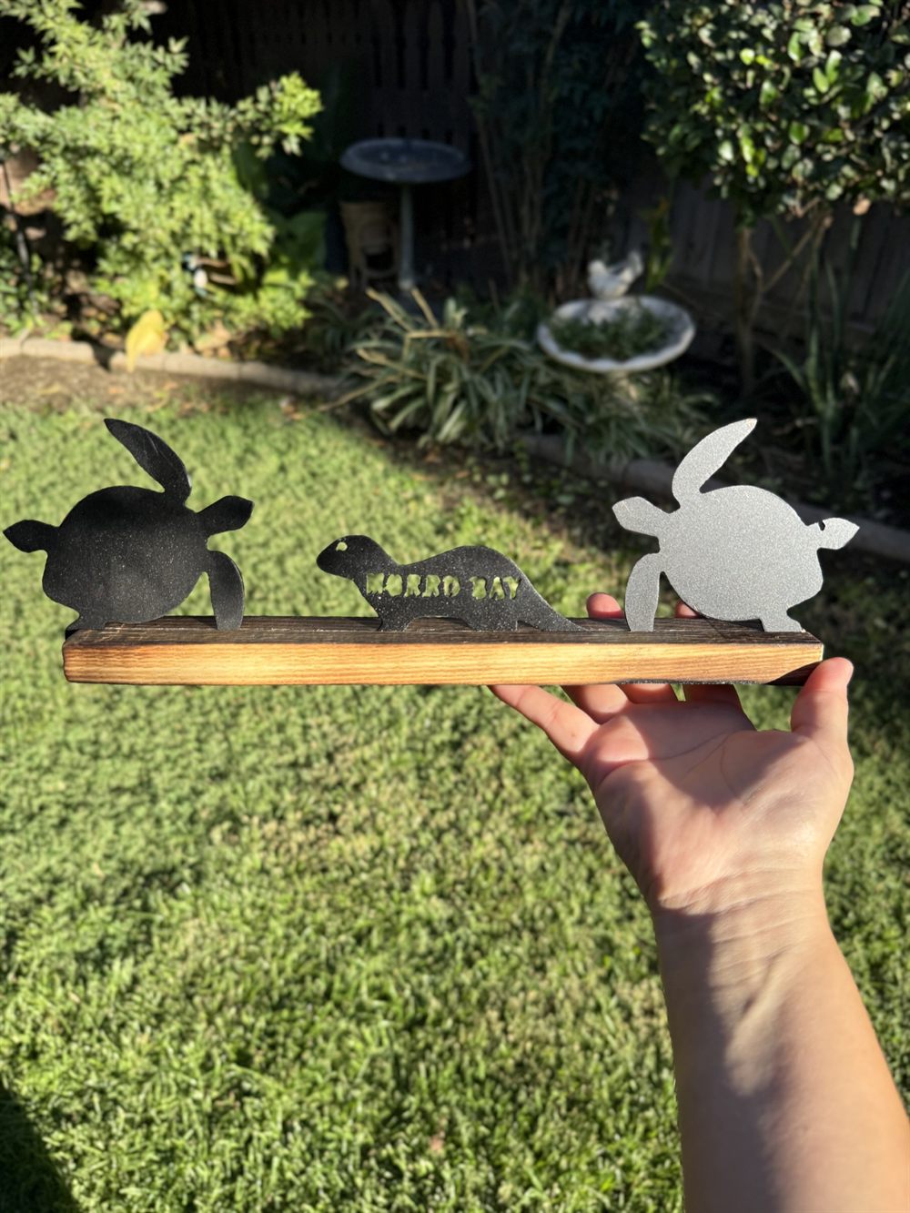 Two turtles and an otter cut from steel on a wood base.