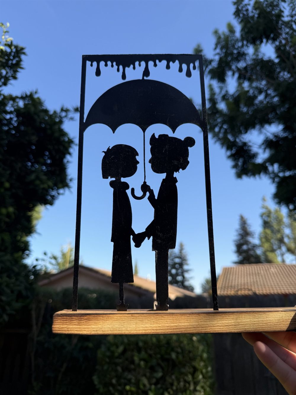 Two figures under an umbrella in the rain, cut from steel.